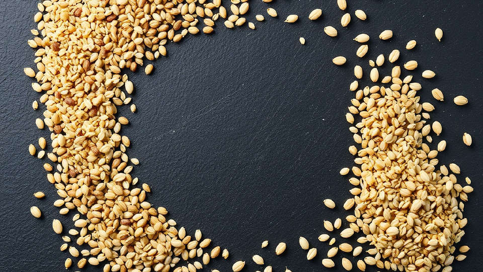 Assorted whole grains scattered on dark slate stone under bright studio lighting
